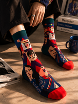 Colorful socks with artistic designs worn by a person sitting on a wooden floor.