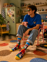 Person sitting in a kitchen wearing colorful socks and holding a mug.