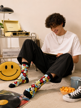 Person sitting on the floor wearing colorful socks with a smiley face design, surrounded by vinyl records and snacks.