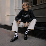 Person wearing a black 'Sporty & Rich' sweatshirt sitting on a step.