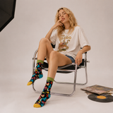Woman sitting on a chair wearing a white t-shirt with colorful socks and denim shorts.