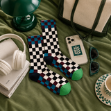 Checkered socks with green accents on a green surface with accessories like headphones, phone, and sunglasses.