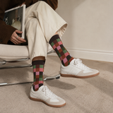 Person wearing patterned socks with white sneakers on a carpeted floor.