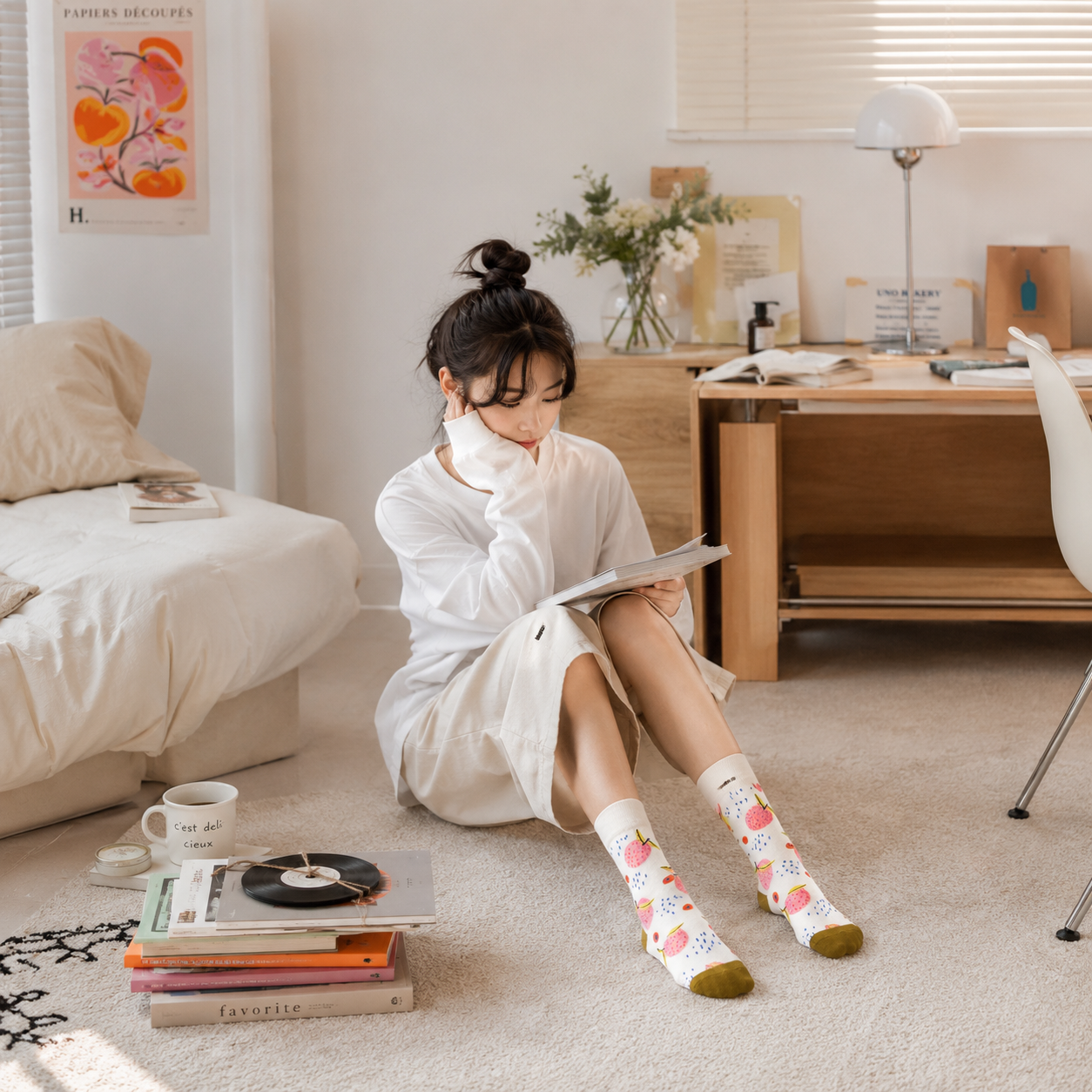 Woman sitting on the floor in a room with books and a desk, wearing floral socks.