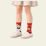Person wearing red socks with cat designs and white sneakers on a plain background