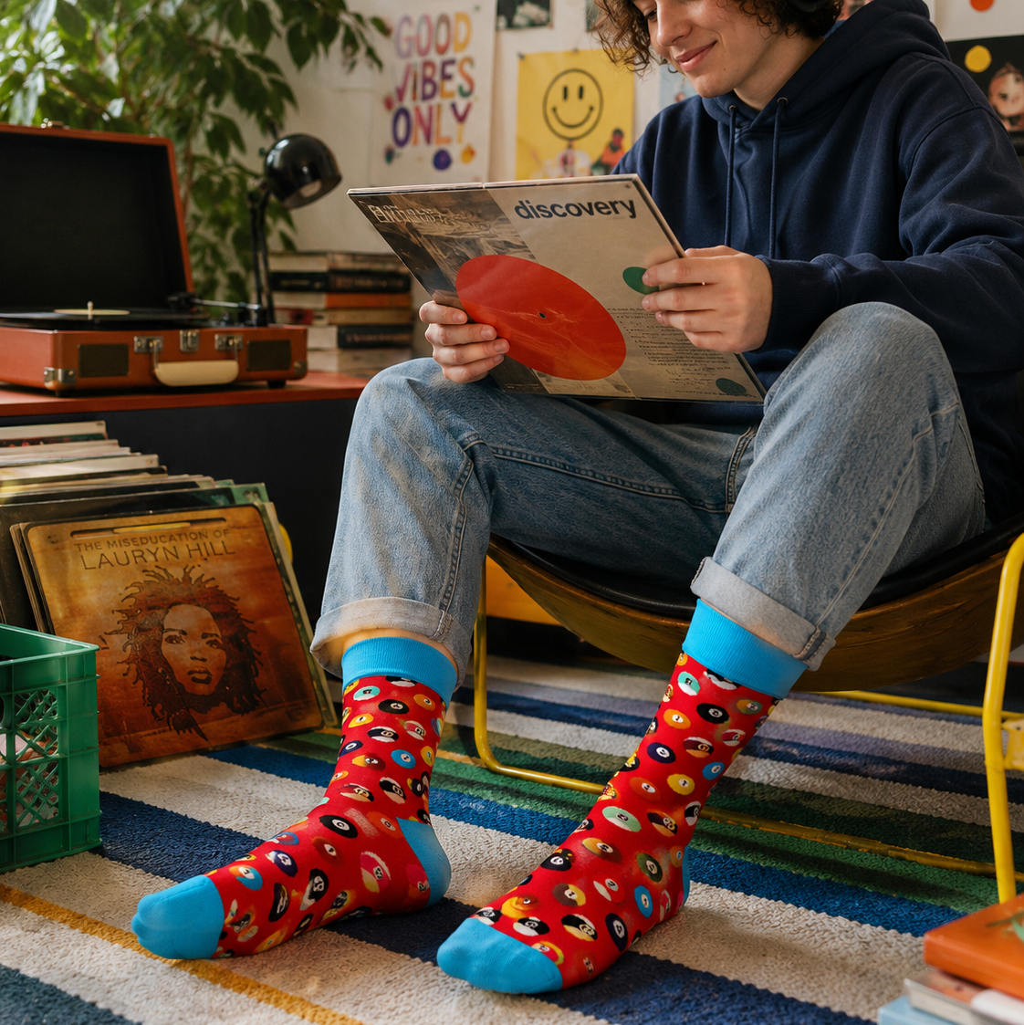 Person wearing colorful socks sitting on a step, holding a record, with a record player and records in the background.