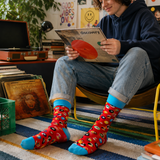 Person wearing colorful socks sitting on a step, holding a record, with a record player and records in the background.
