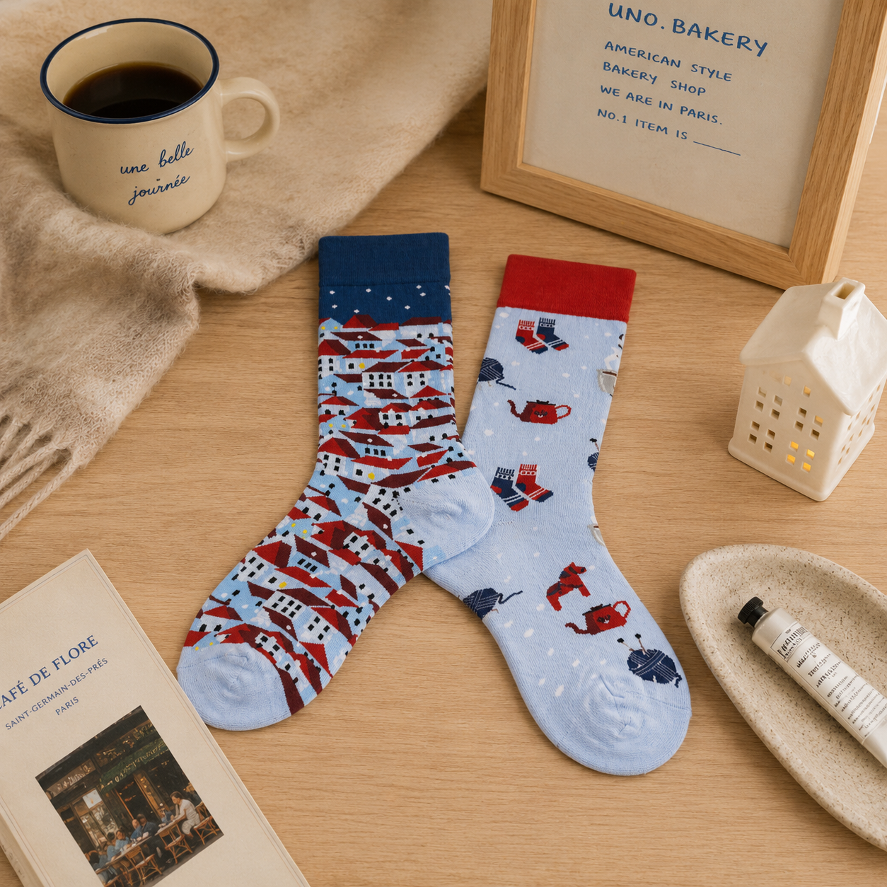 Two patterned socks on a wooden surface with a mug, book, and small lamp.