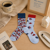 Two patterned socks on a wooden surface with a mug, book, and small lamp.