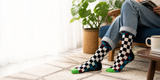 Person wearing colorful checkered socks sitting on a couch with a plant and coffee mug in the background.