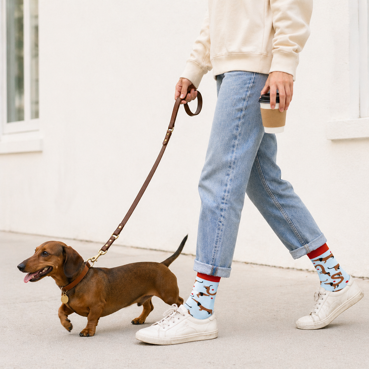 Person walking a dog on a leash with a cup in hand, wearing patterned socks.