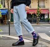 Person wearing light blue jeans and black shoes with pink flamingo socks on a city street.